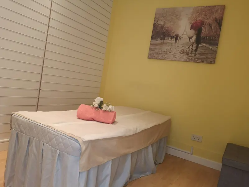 Treatment room two with a massage table, rolled pink towel and white roses